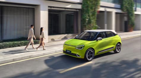 Yellow Dongfeng Box urban electric car with white roof driving through the city, front and side view